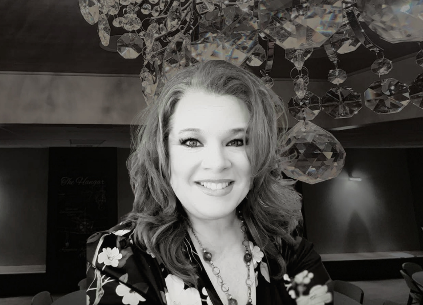 Smiling woman in floral top under a crystal chandelier, in a dimly lit room.