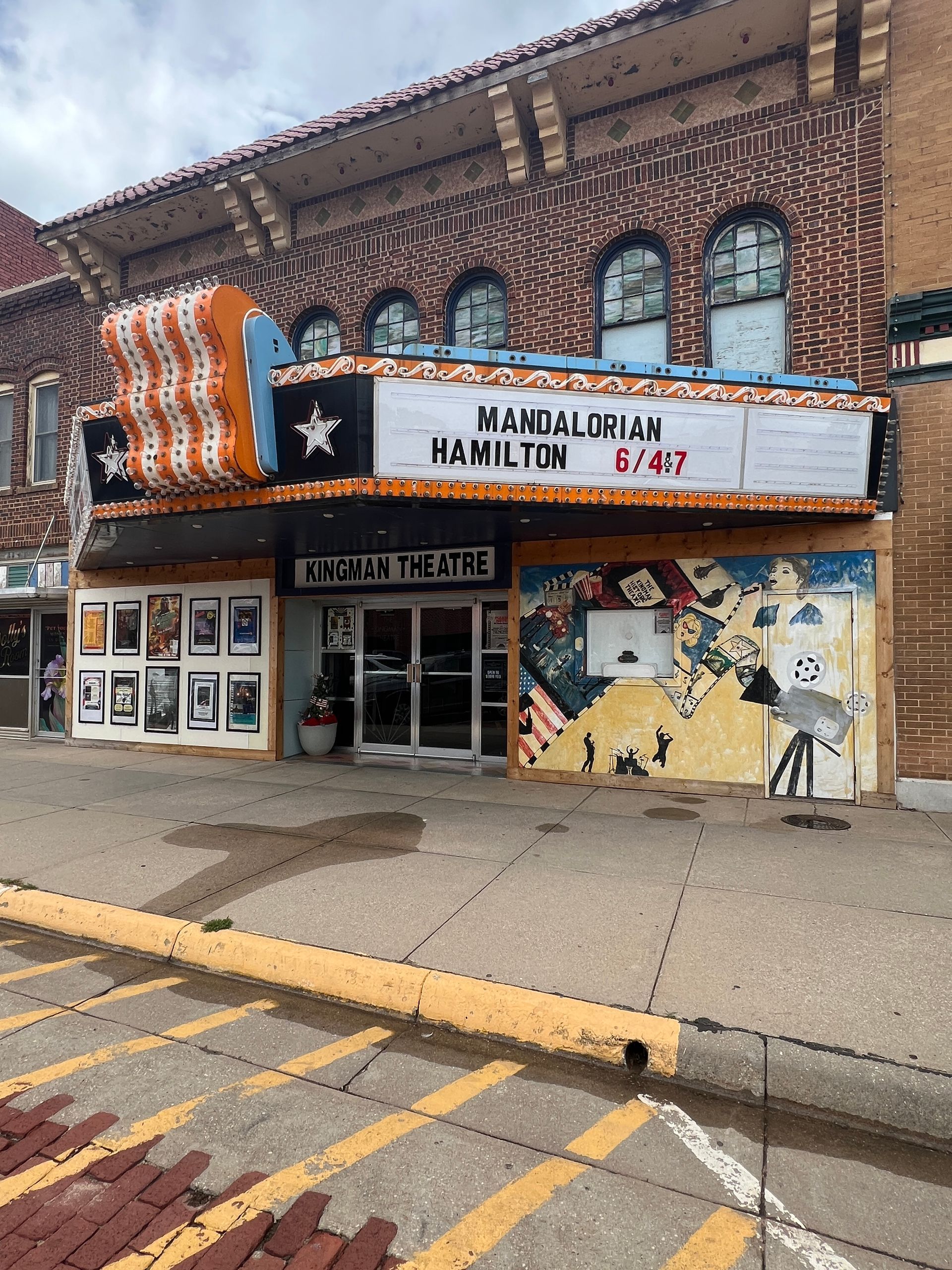 Exterior of Hamilton theater with brick facade, blue awning, and colorful mural beside a sidewalk and street markings