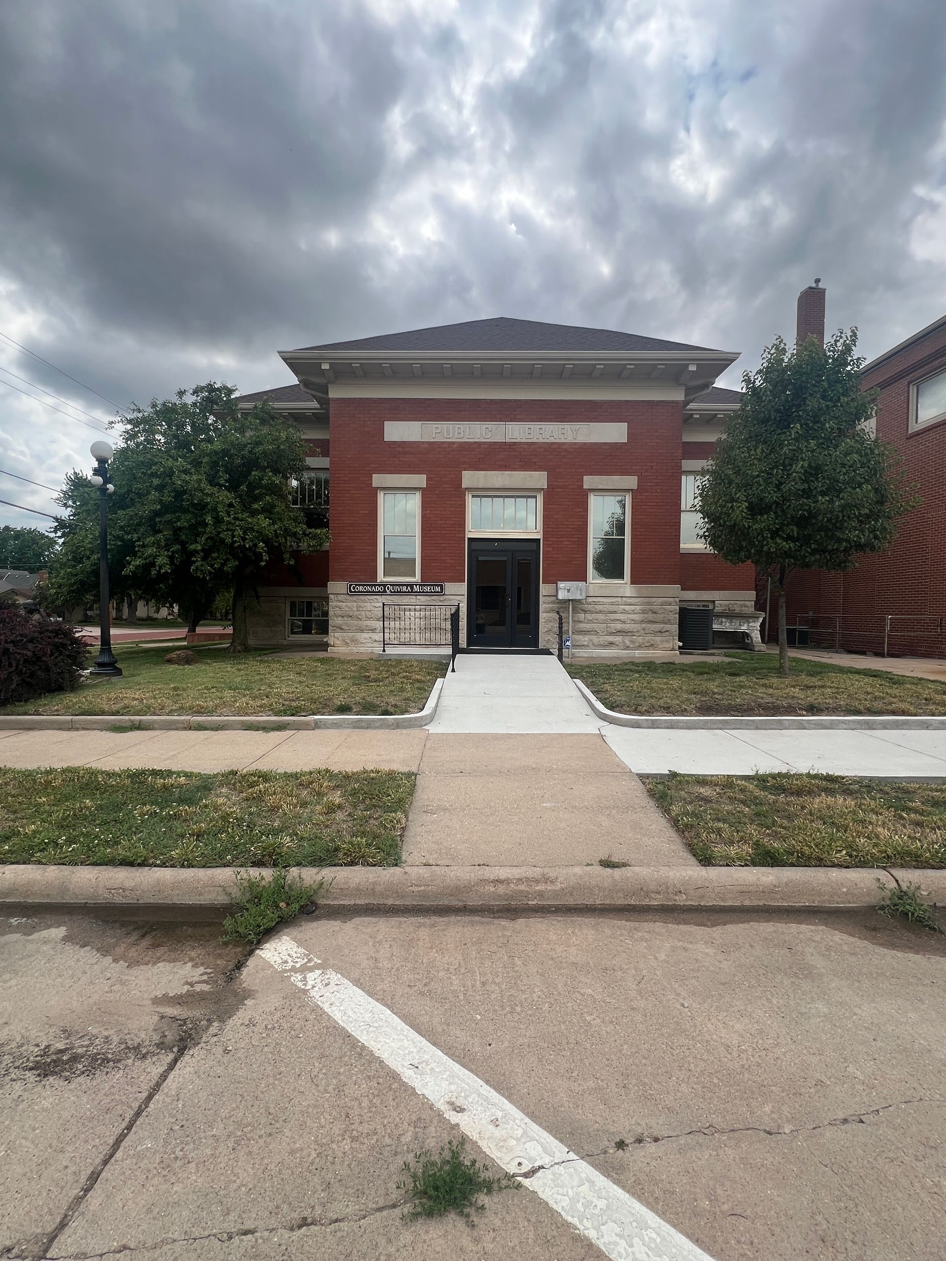 Red brick building with a central entrance, white trim, and a sidewalk under a cloudy sky.