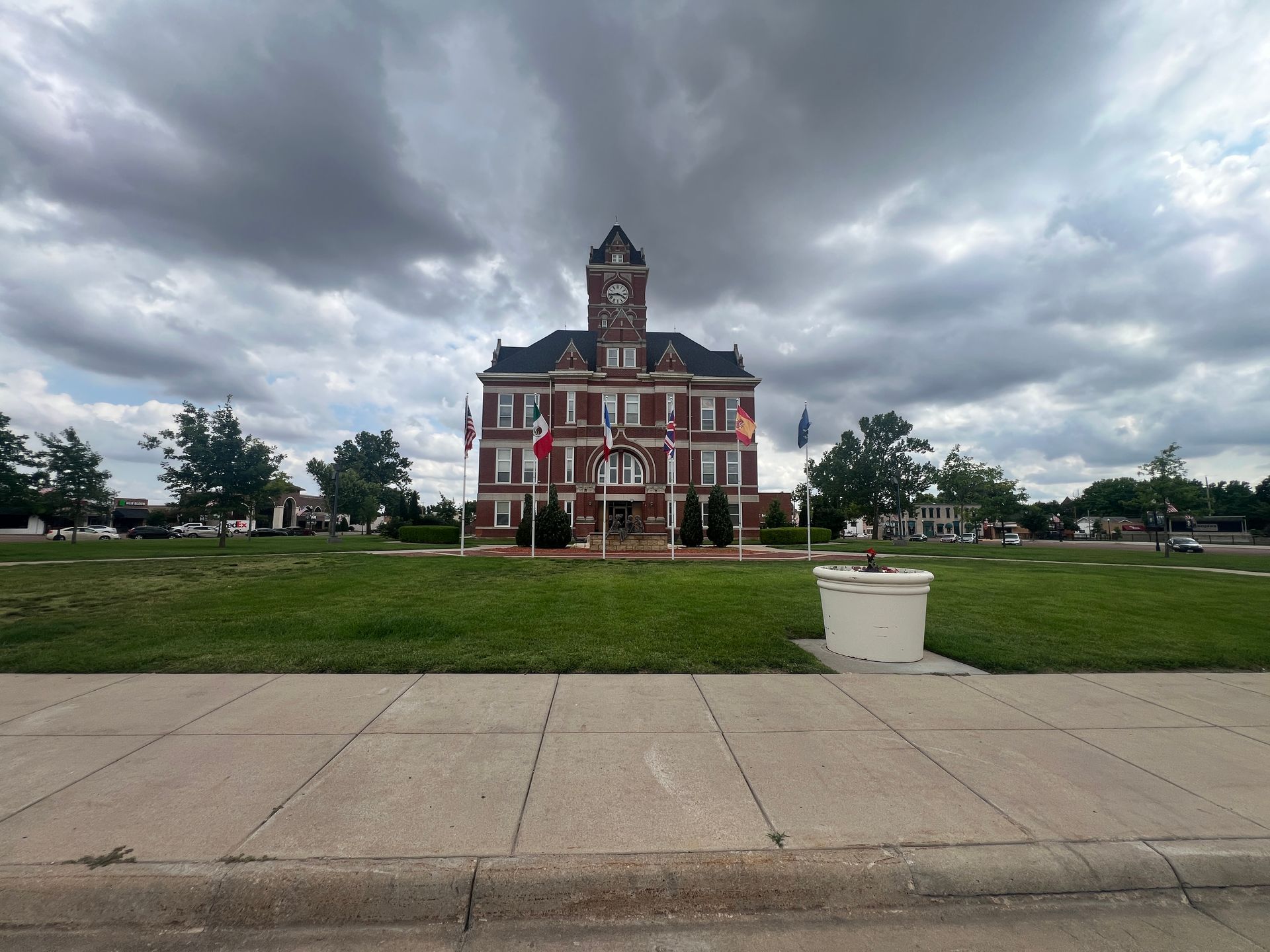 Historic red-brick courthouse on a grassy lawn under cloudy sky, viewed from a sidewalk