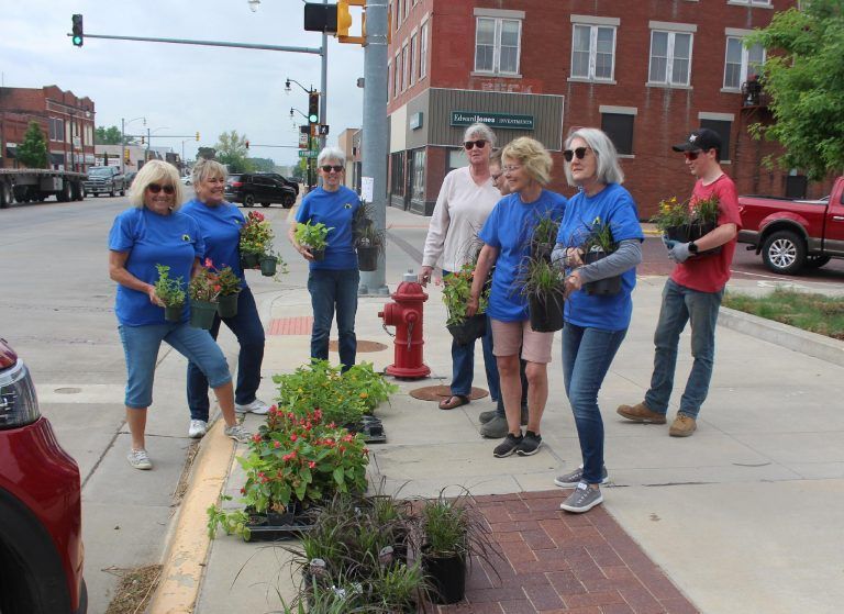 Volunteers in blue shirts planting flowers along a city sidewalk near an intersection