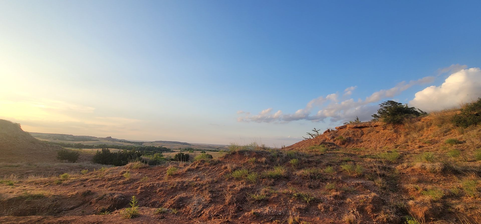Sunlit rocky hillside overlooking a valley at sunset with blue sky and scattered clouds
