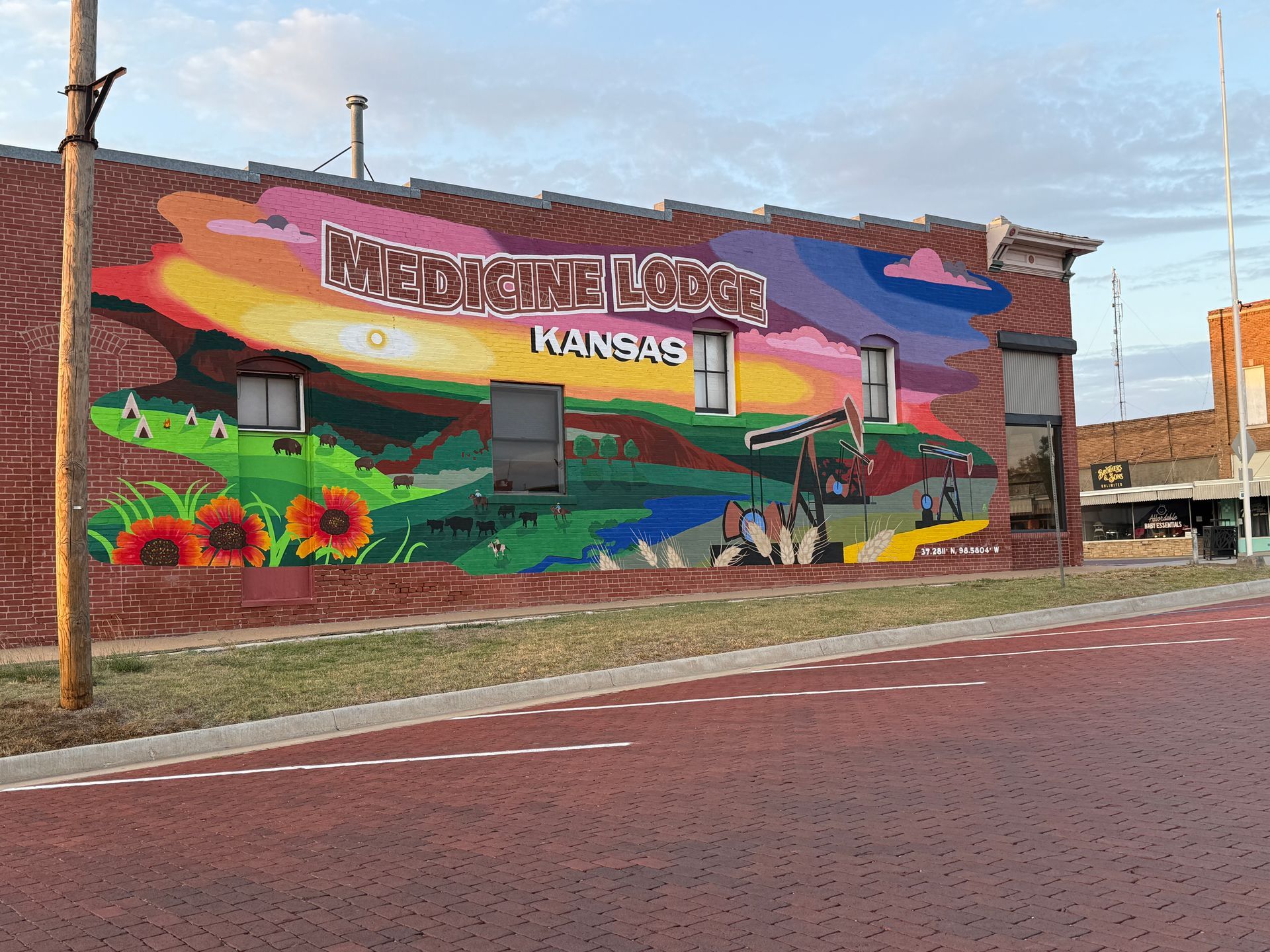 Colorful mural on a brick wall reading βNorton, Kansas,β beside a red street and sidewalk.