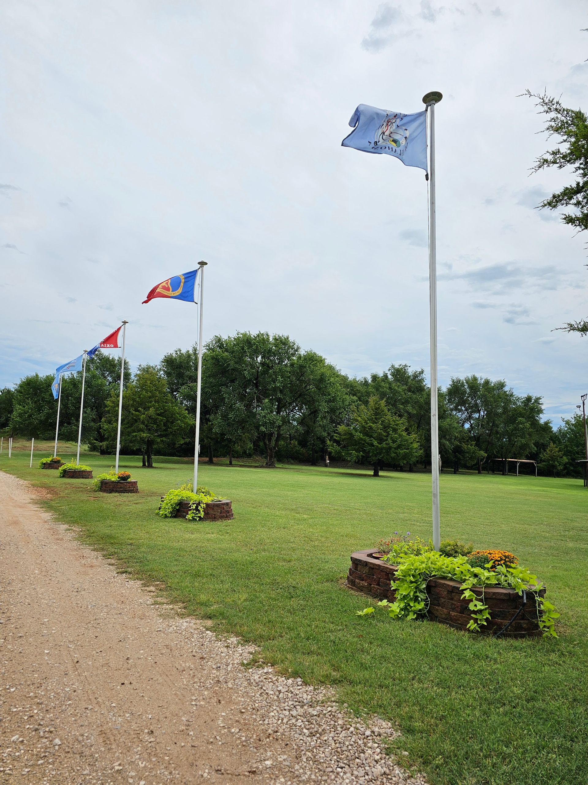 Flags on white poles along a gravel path in a grassy field under a cloudy sky