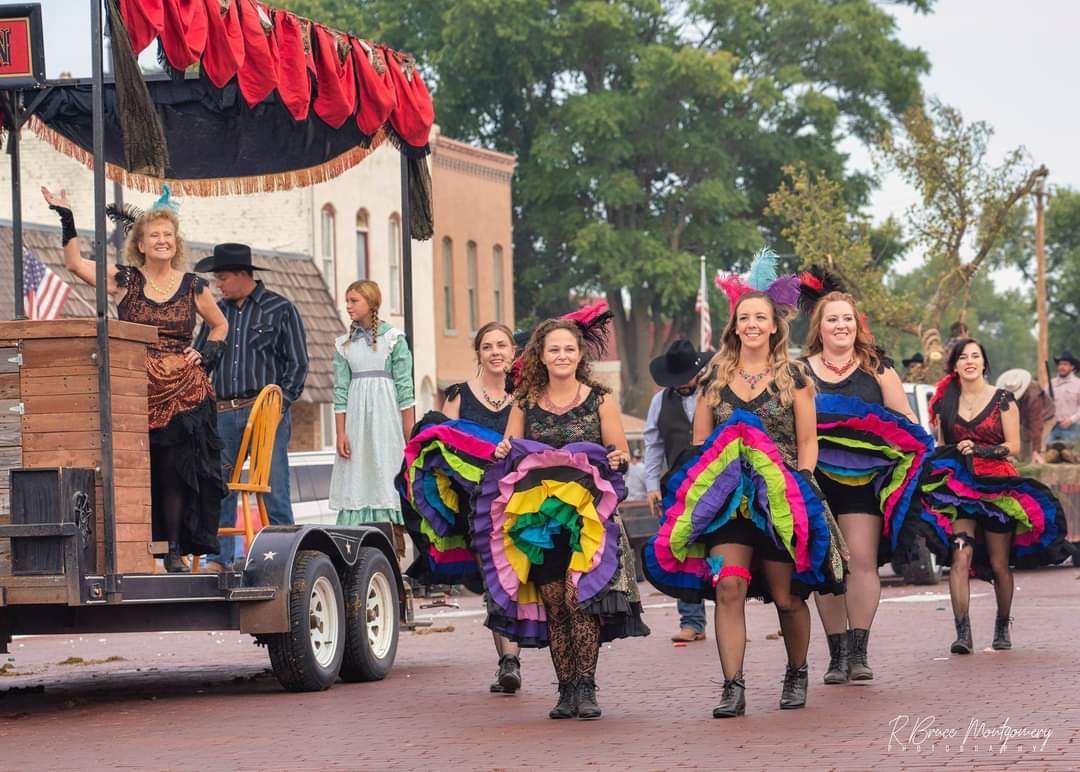 Parade dancers in rainbow skirts perform beside a decorated float on a street