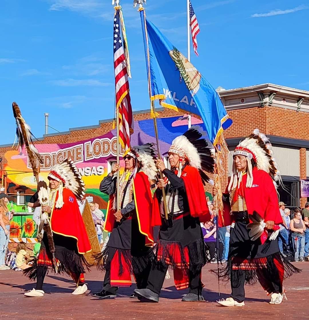Parade performers in red and black regalia walk with flags in a sunny street festival