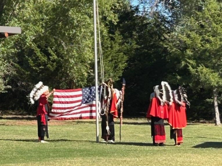 Honor guard in red uniforms standing beside an American flag on a grassy field