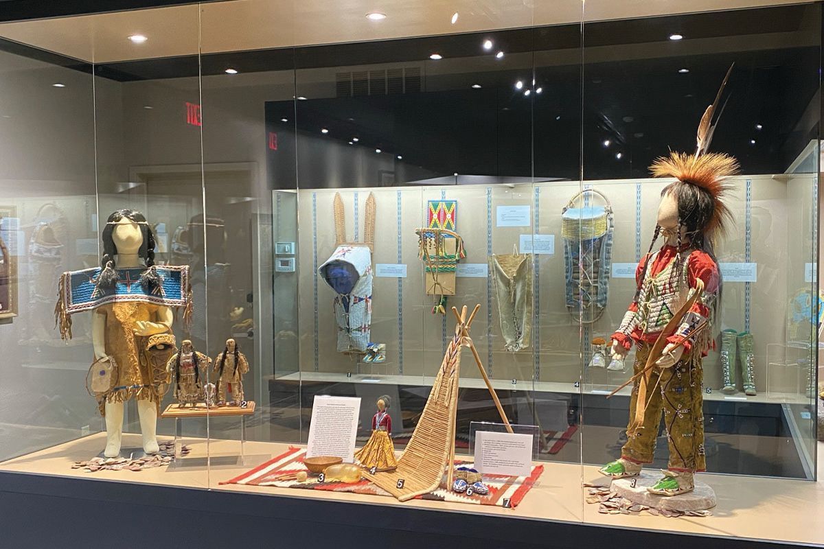 Museum display of ornate cultural costumes and masks in a glass case, with gold and red garments on mannequins