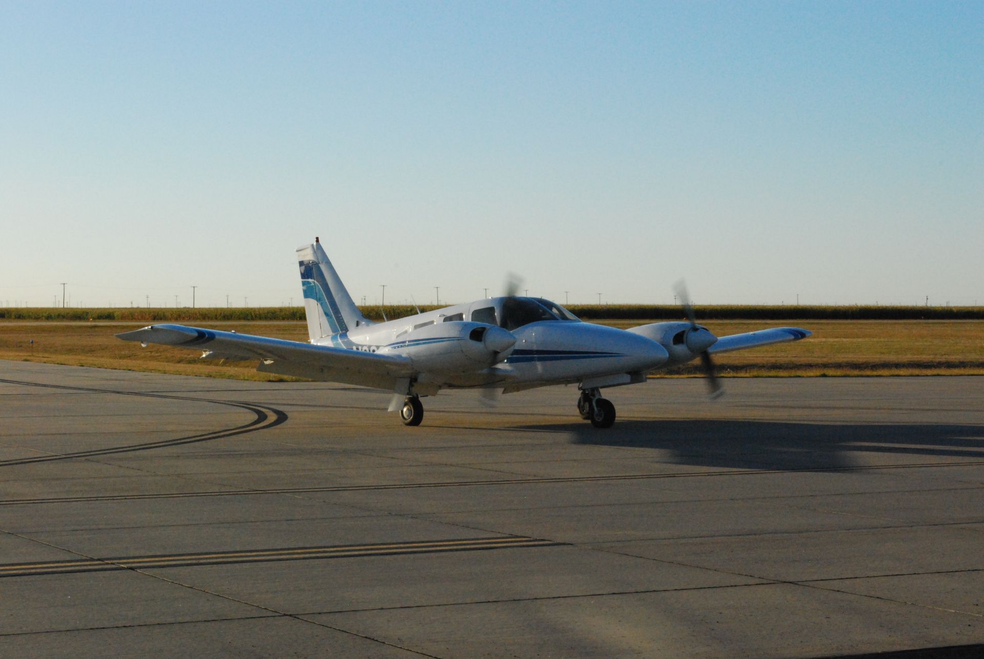 Small twin-engine airplane on a runway at sunset, with blue-and-white tail and clear sky.