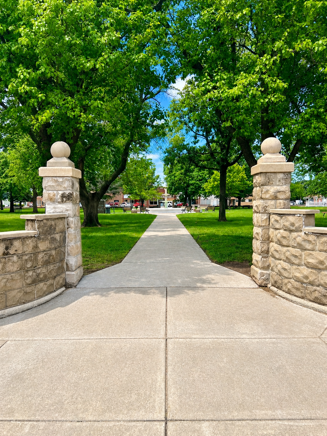 Stone gate opening to a tree-lined park path on a sunny day