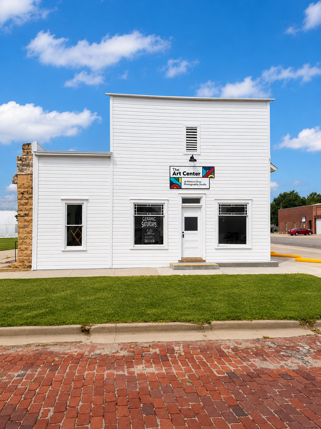 White storefront with a red, white, and blue sign on a brick street under a blue sky