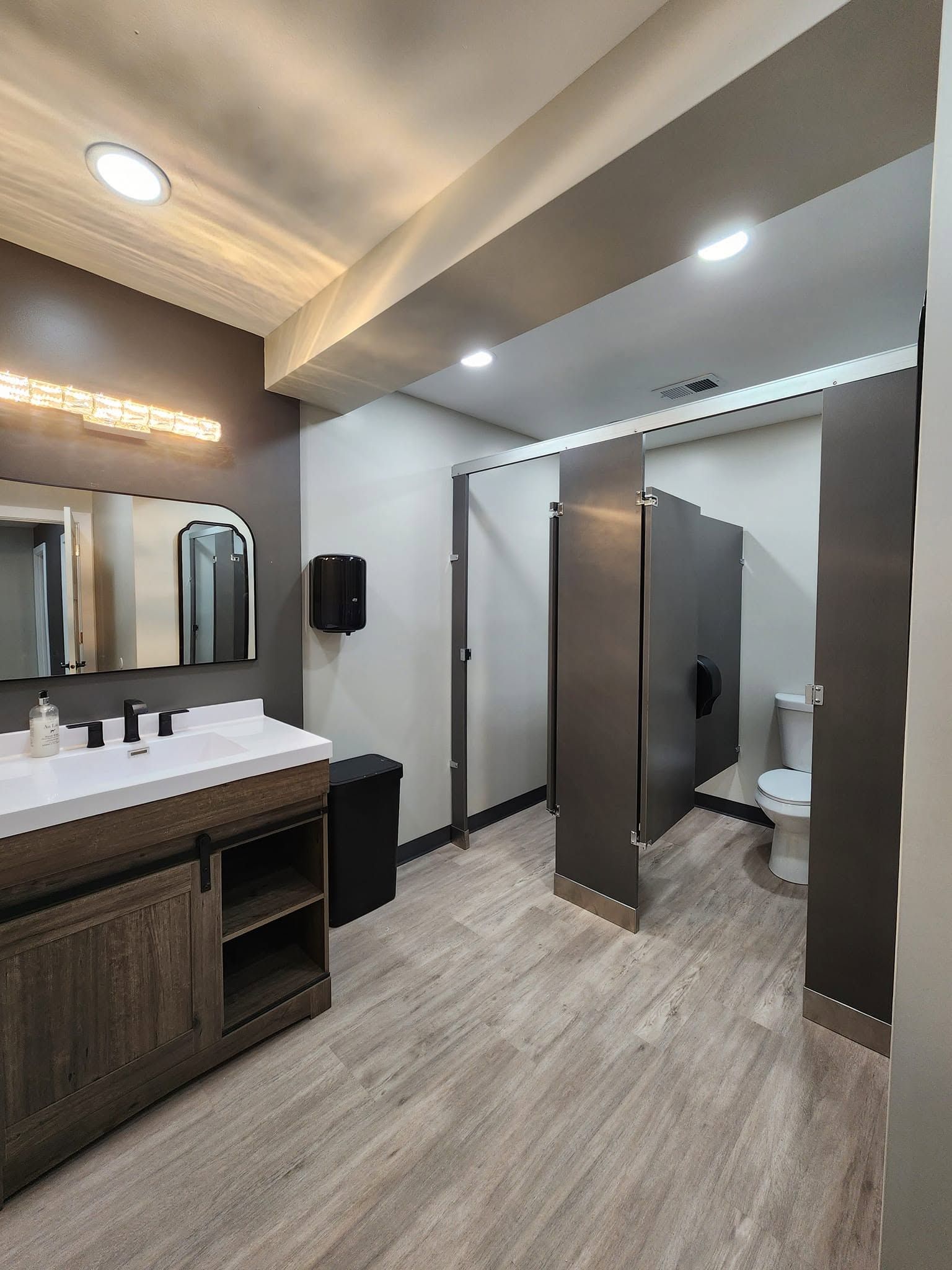 Modern public restroom with sinks, mirrors, stalls, and wood-accented finishes.