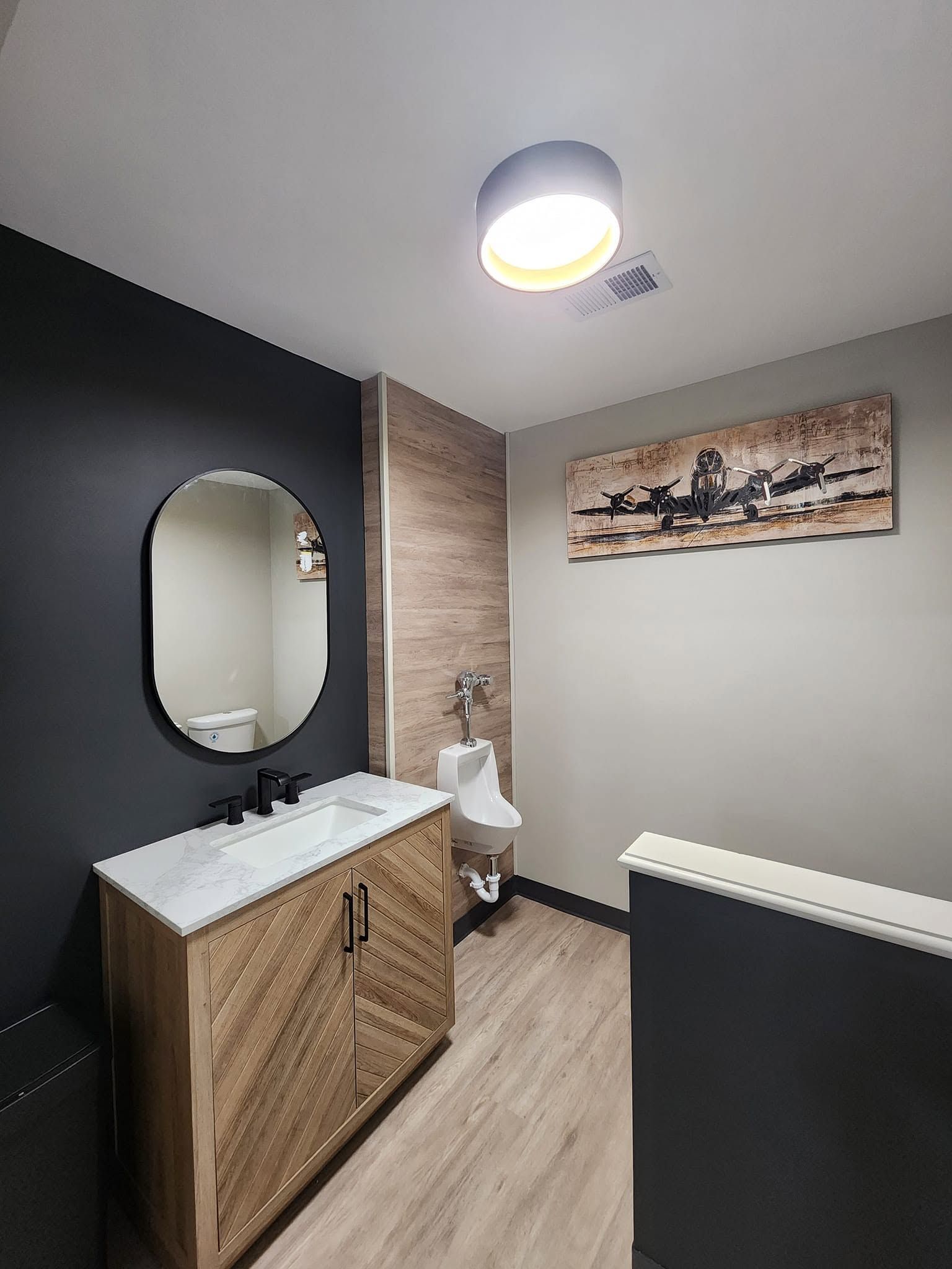 Small bathroom with dark walls, wood vanity, round mirror, toilet, and wall art.