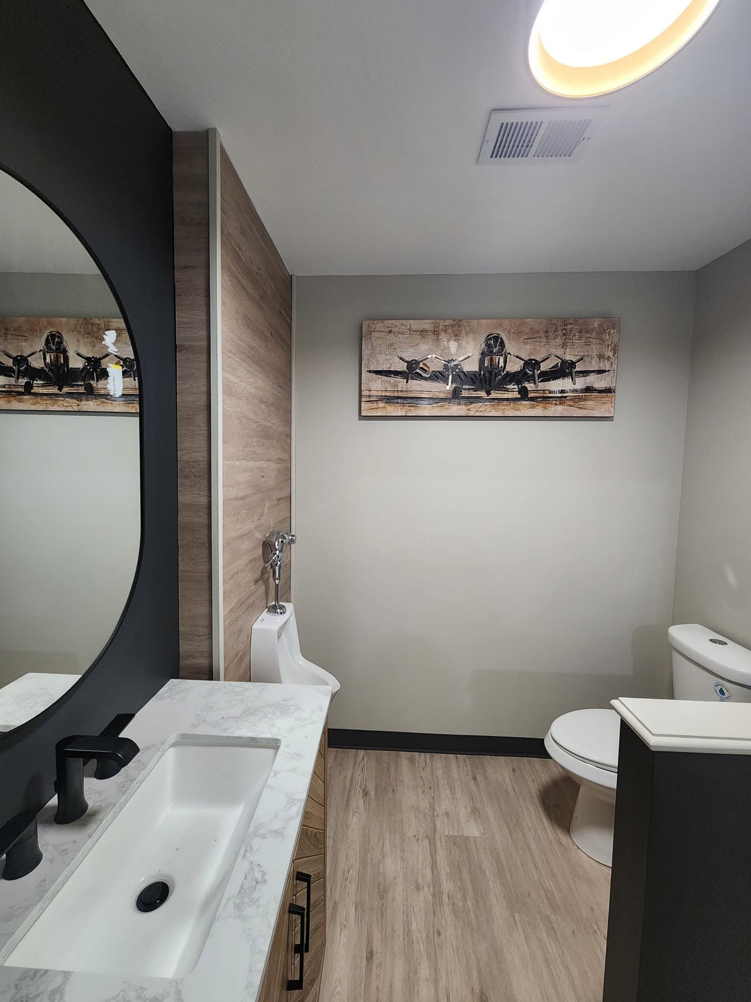 Small modern bathroom with sink, toilet, shower, and wall art in neutral tones.