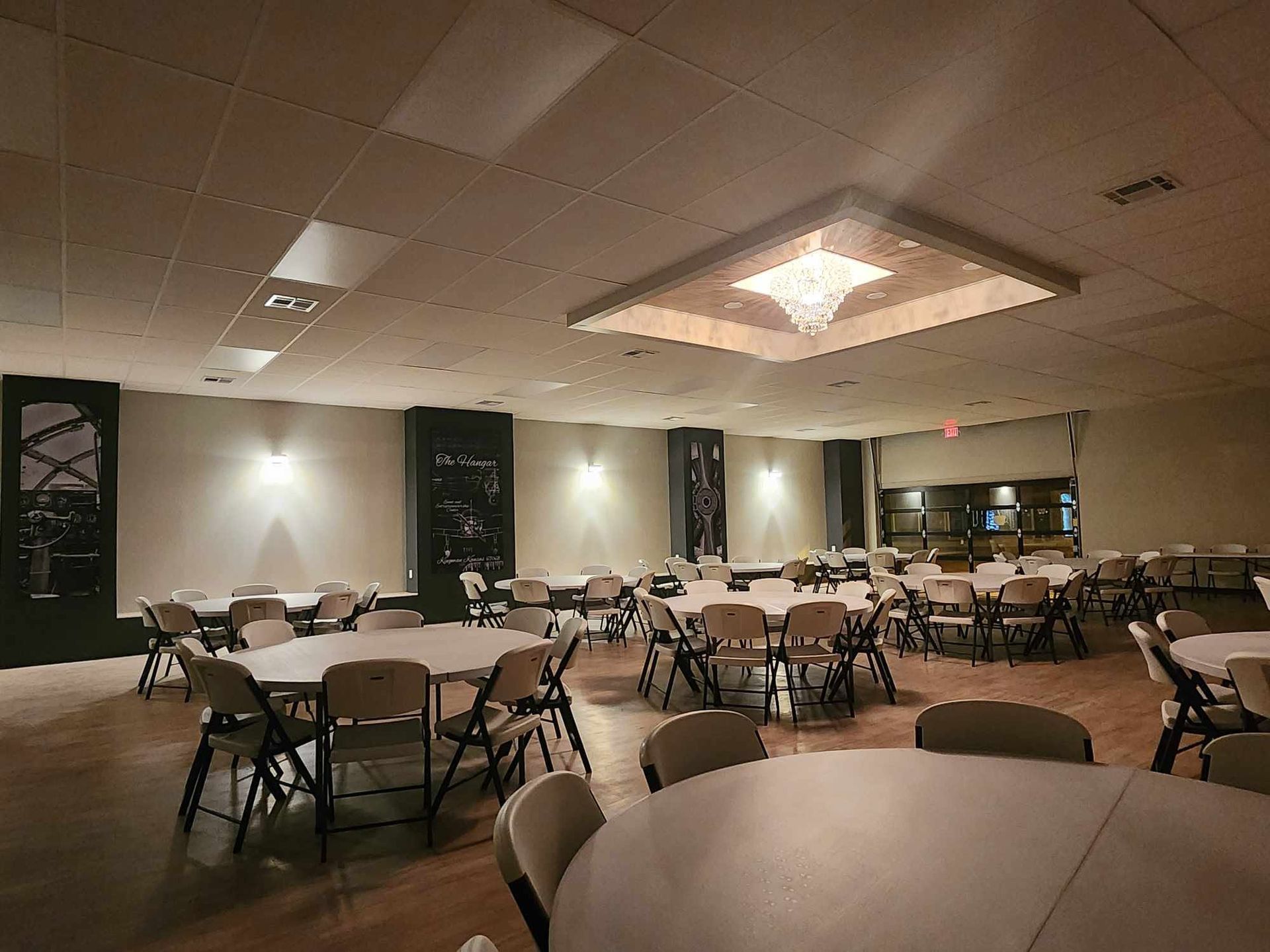Empty banquet hall with round tables, folding chairs, and warm ceiling lights