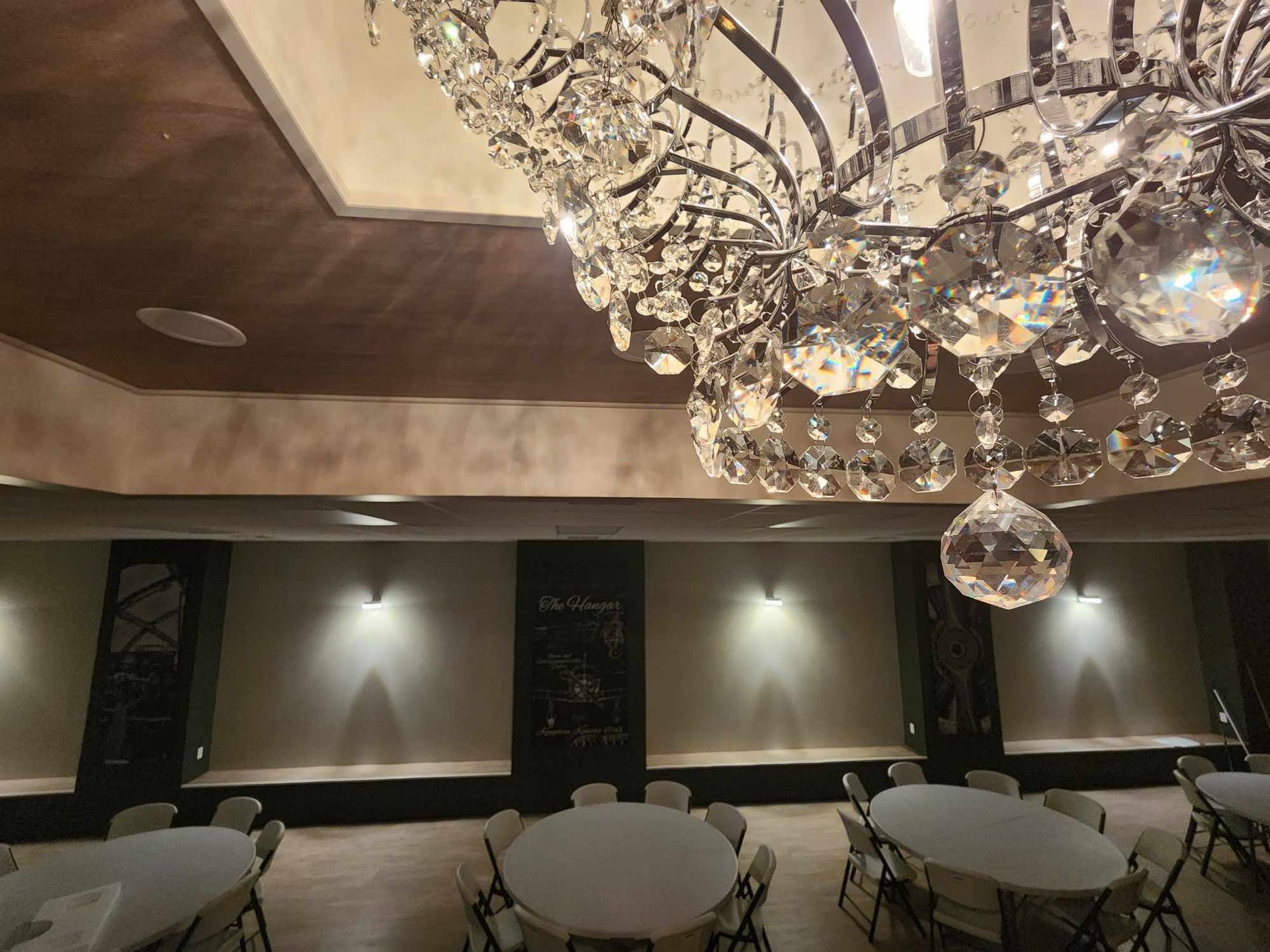 Elegant banquet hall with crystal chandeliers, round tables, and a projection screen at the front.