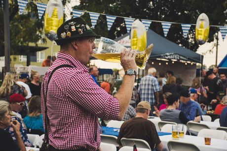 Man in pink checkered shirt blows a brass horn at an outdoor festival crowd