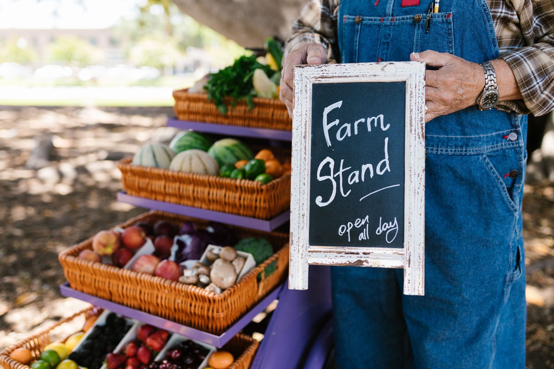 Farm stand sign beside baskets of fresh produce and vegetables outdoors
