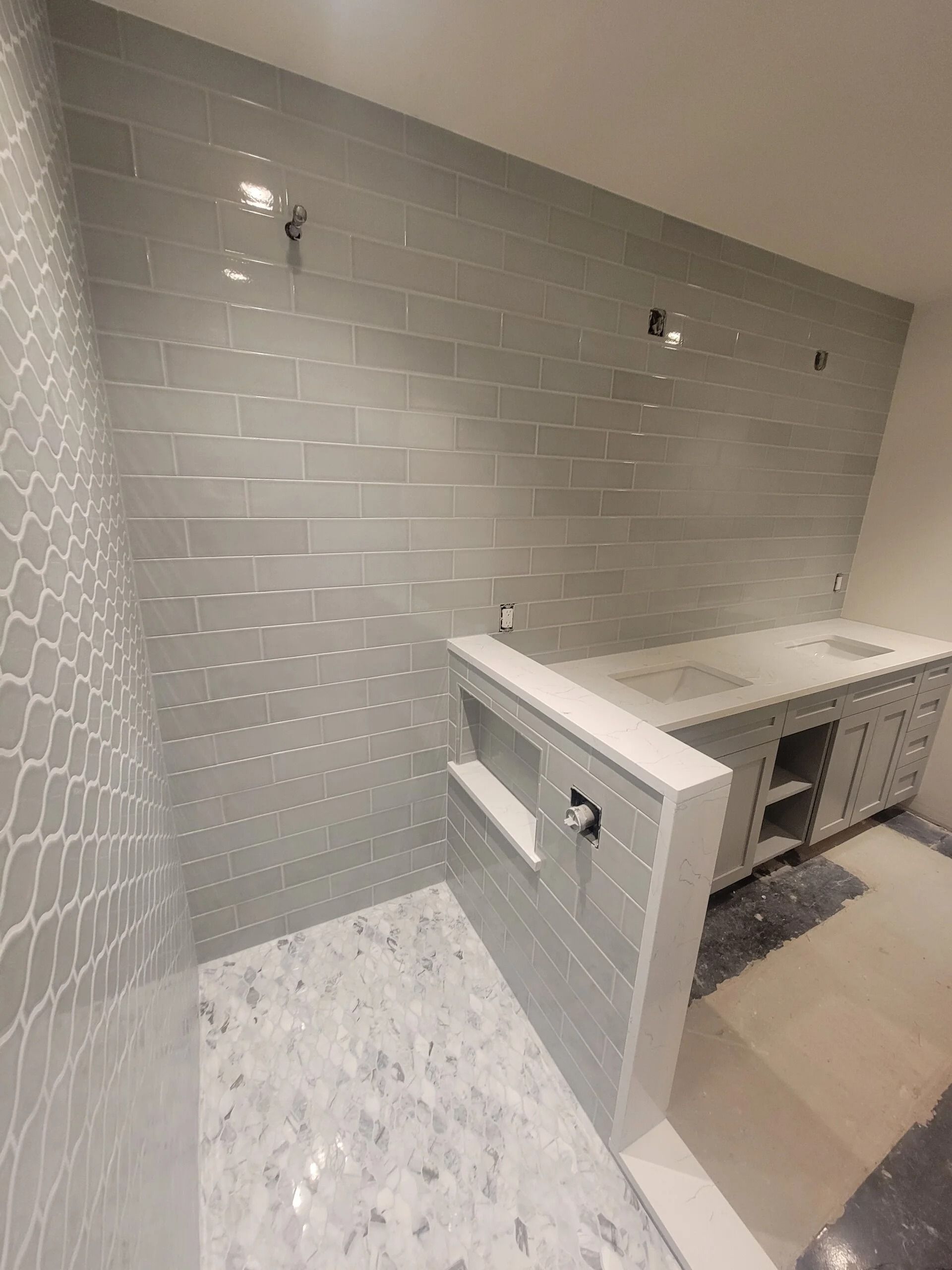 Bathroom with gray tiled shower and vanity under construction.