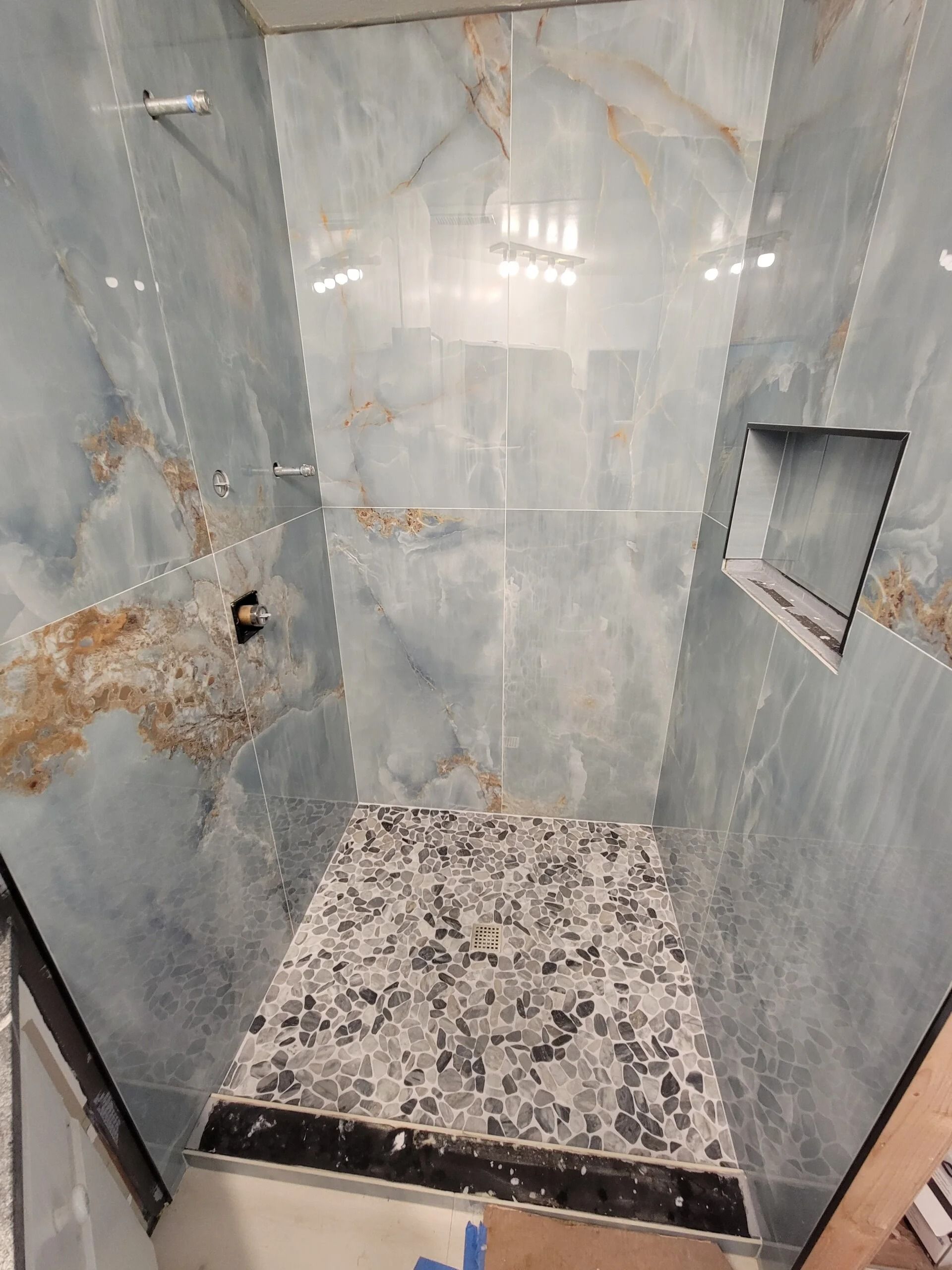 Blue-tiled shower with a mosaic floor. The walls have brown veining. Built-in shelf, showerhead, and drain.