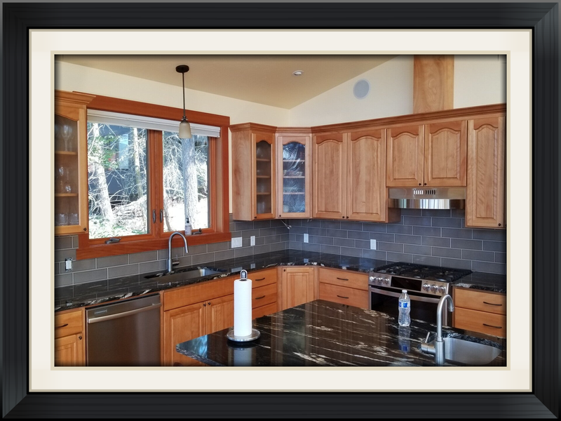 Kitchen with wood cabinets, dark countertops, and stainless steel appliances; window view of trees.