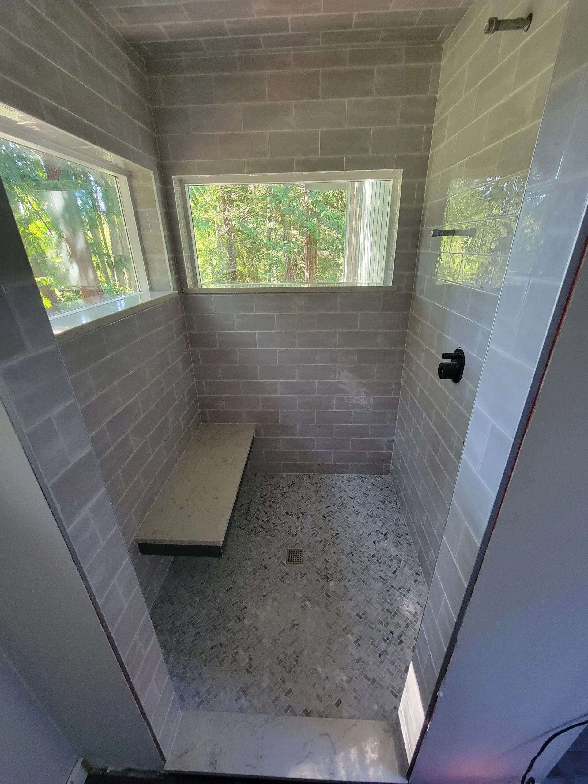 Gray tiled shower with a bench and windows.