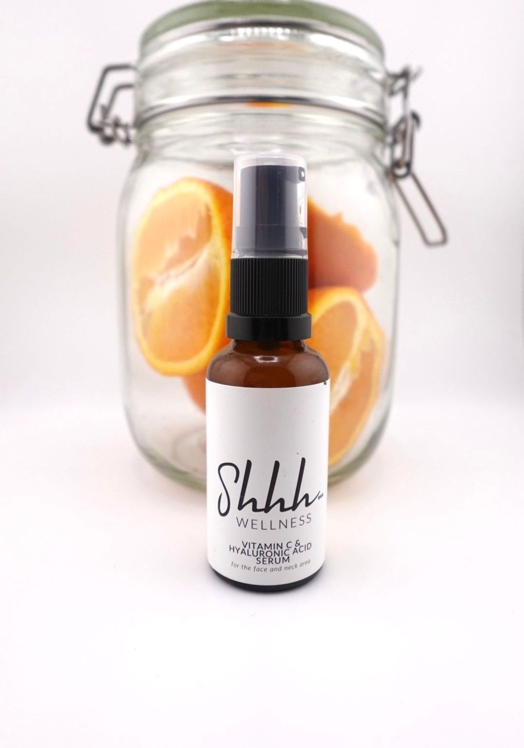 Brown spray bottle with white label, in front of a glass jar with oranges inside.