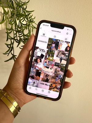 Hand holding a smartphone displaying an Instagram profile with photo and posts, outdoors.