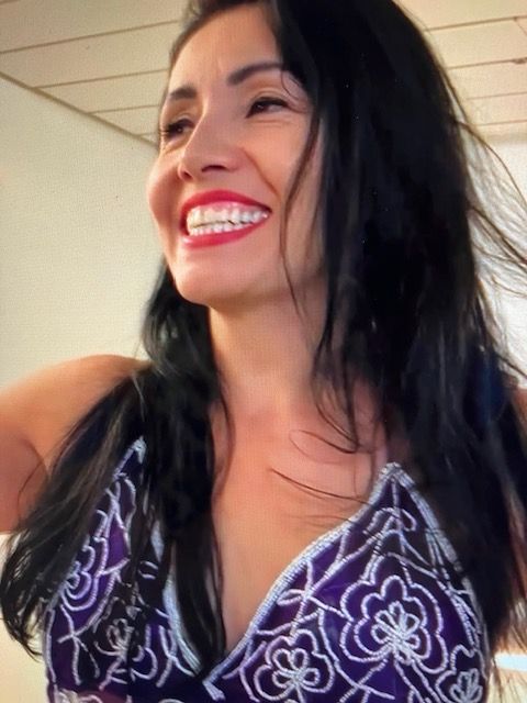 A woman in a purple top is smiling with her hair blowing in the wind.