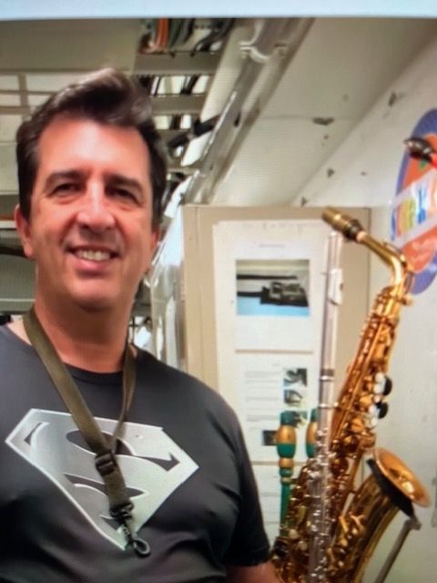 A man wearing a superman shirt is holding a saxophone