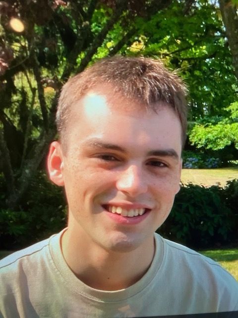 A young man is smiling for the camera in front of trees