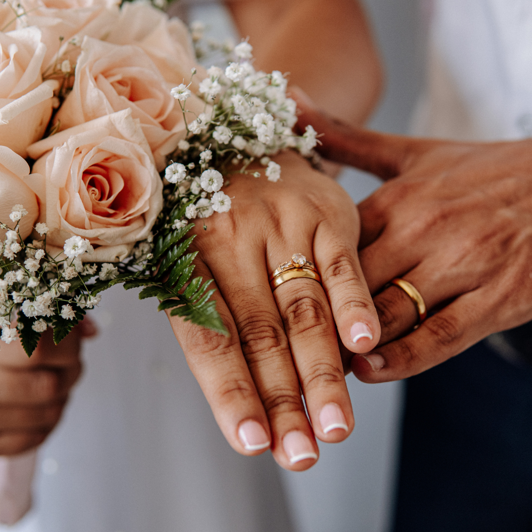 Close-up of hands with wedding rings, holding a bouquet of pink roses.