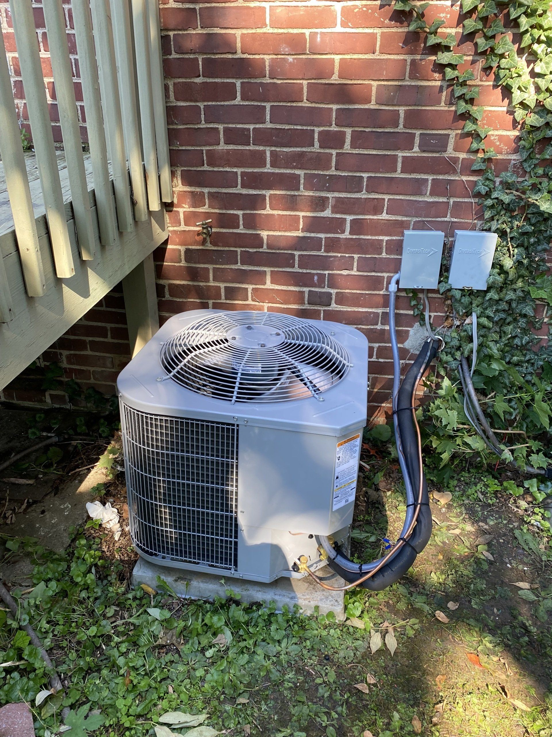 An air conditioner is sitting in the grass next to a brick wall.