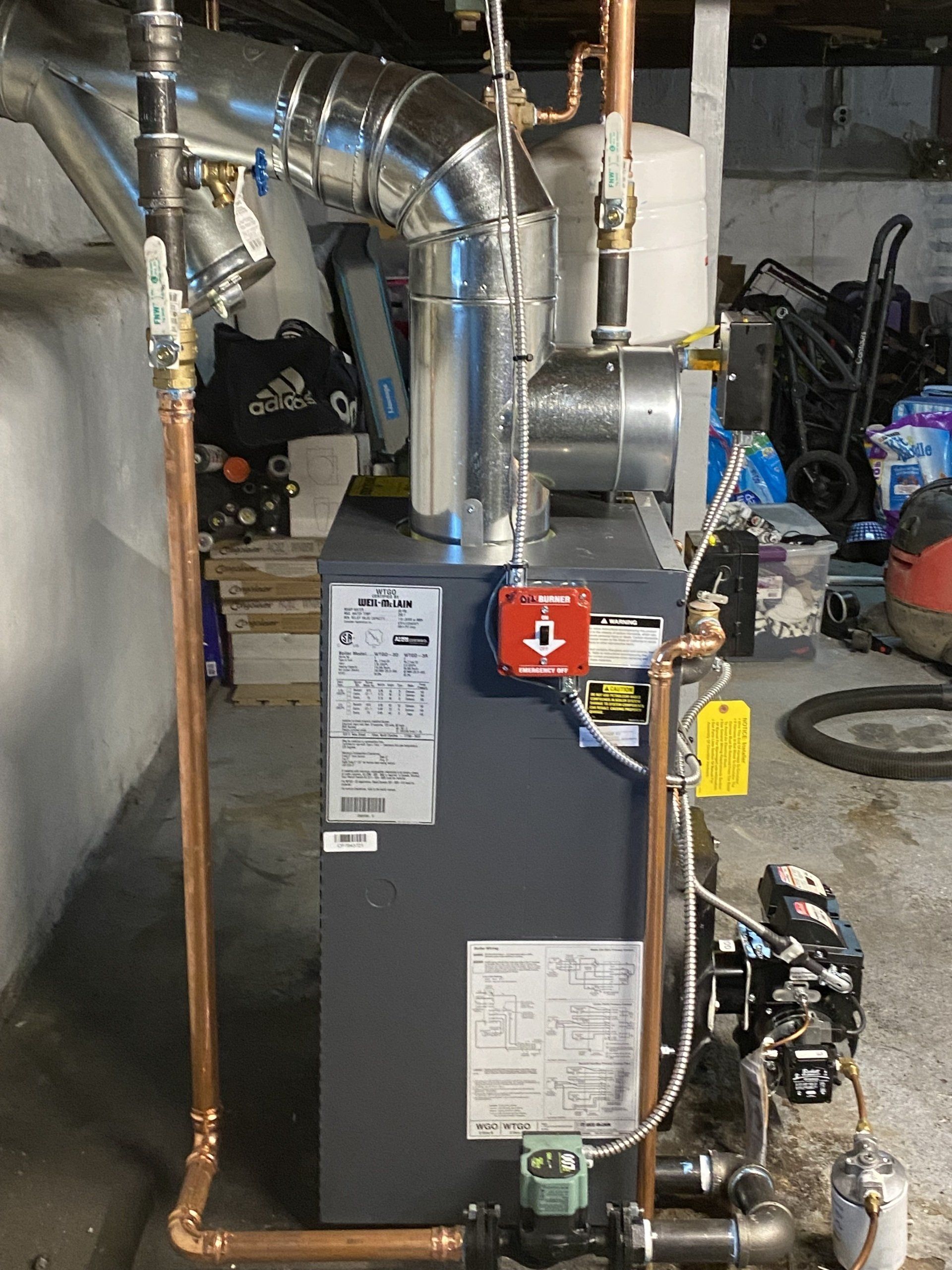 A boiler with copper pipes attached to it is sitting in a basement.