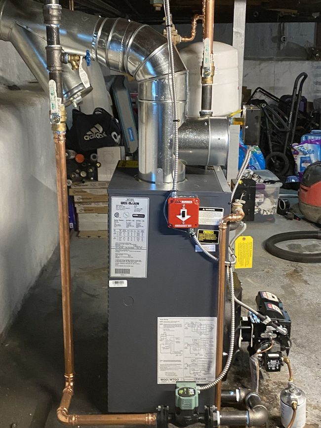 A boiler with copper pipes attached to it is sitting in a basement.