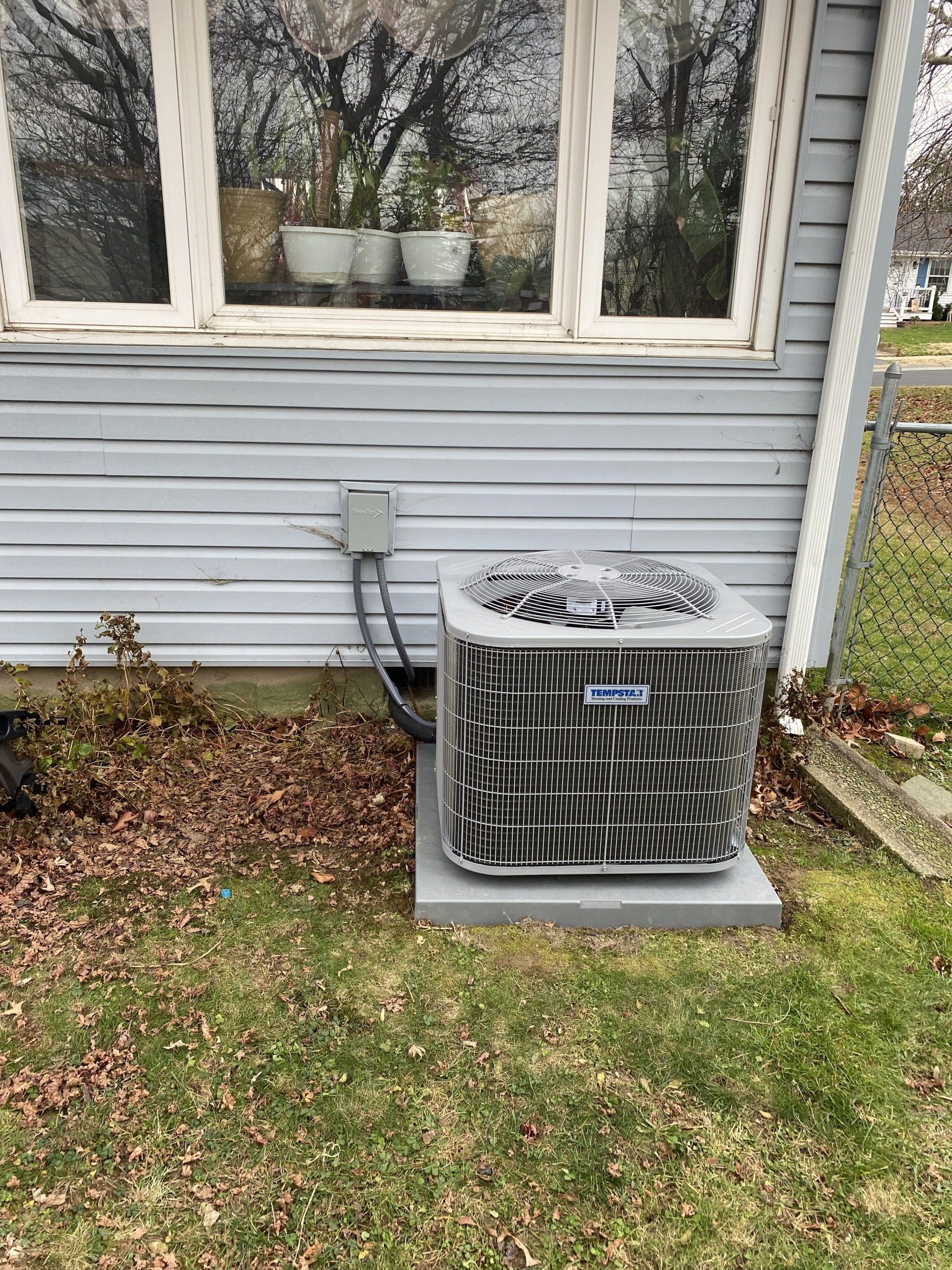 An air conditioner is sitting on the side of a house next to a window.