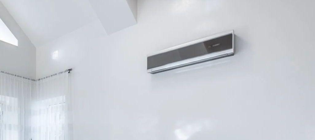 A wall mounted air conditioner is hanging on a white wall in a room.