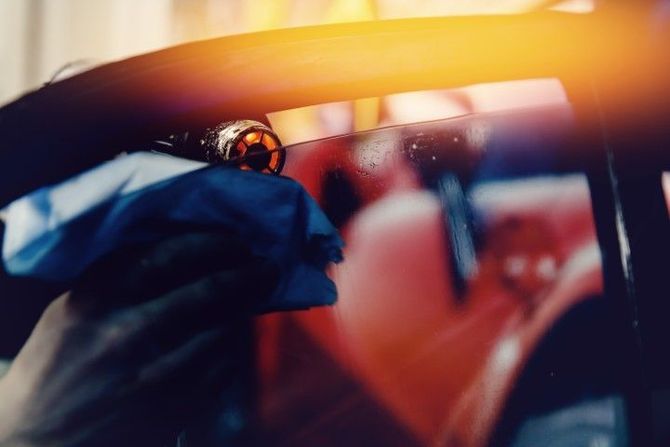 Close-up of a person gripping a steering wheel in a car, with warm sunlight and blurred reflections.