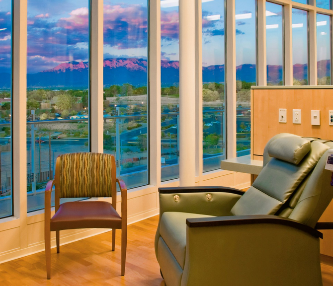 Modern room with large windows, two chairs, and a view of water and mountains at sunset