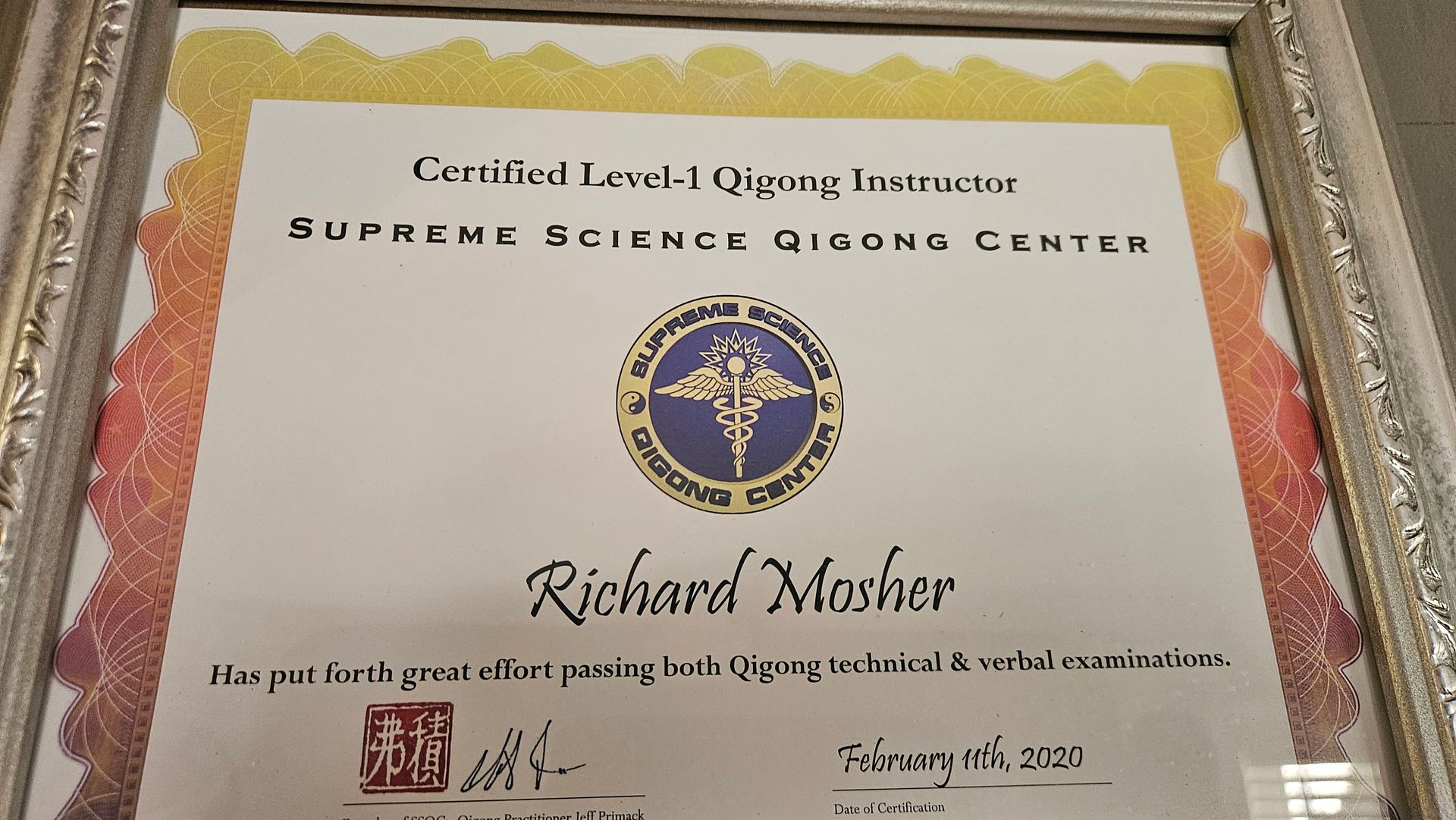 Certificate for Richard Mosher from Supreme Science Qigong Center, bordered in gold on a table