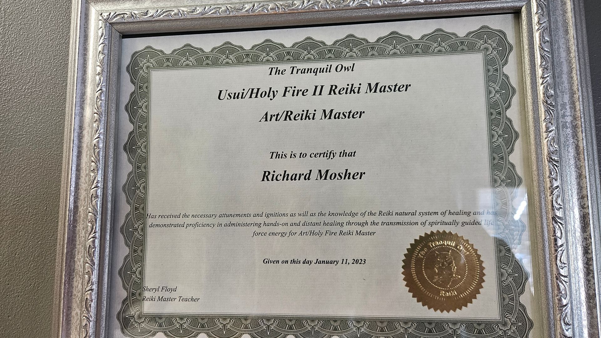 Framed certificate with ornate silver border and gold seal, displayed on a wall.