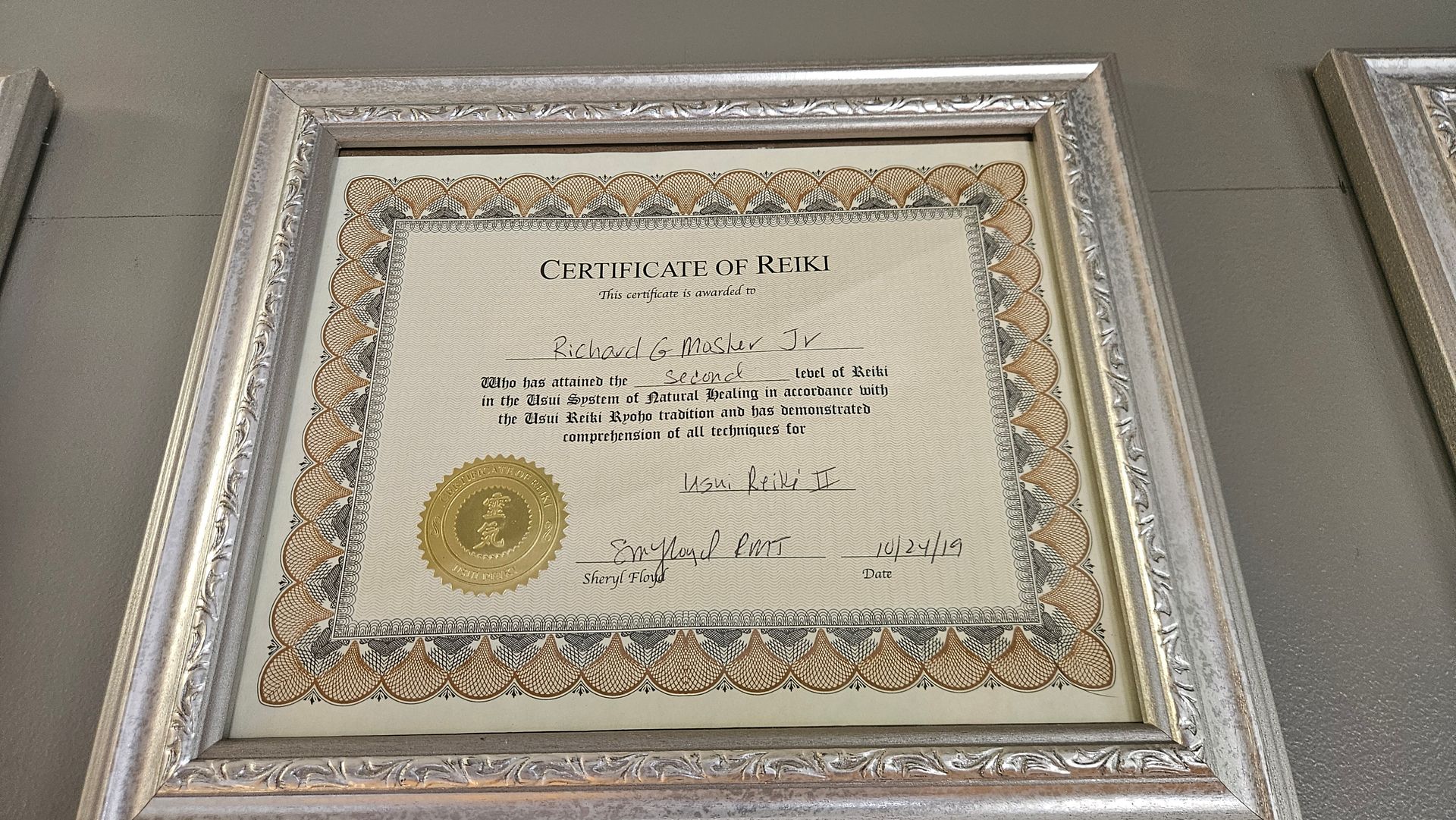 Framed certificate with ornate border and gold seal, hanging on a wall.