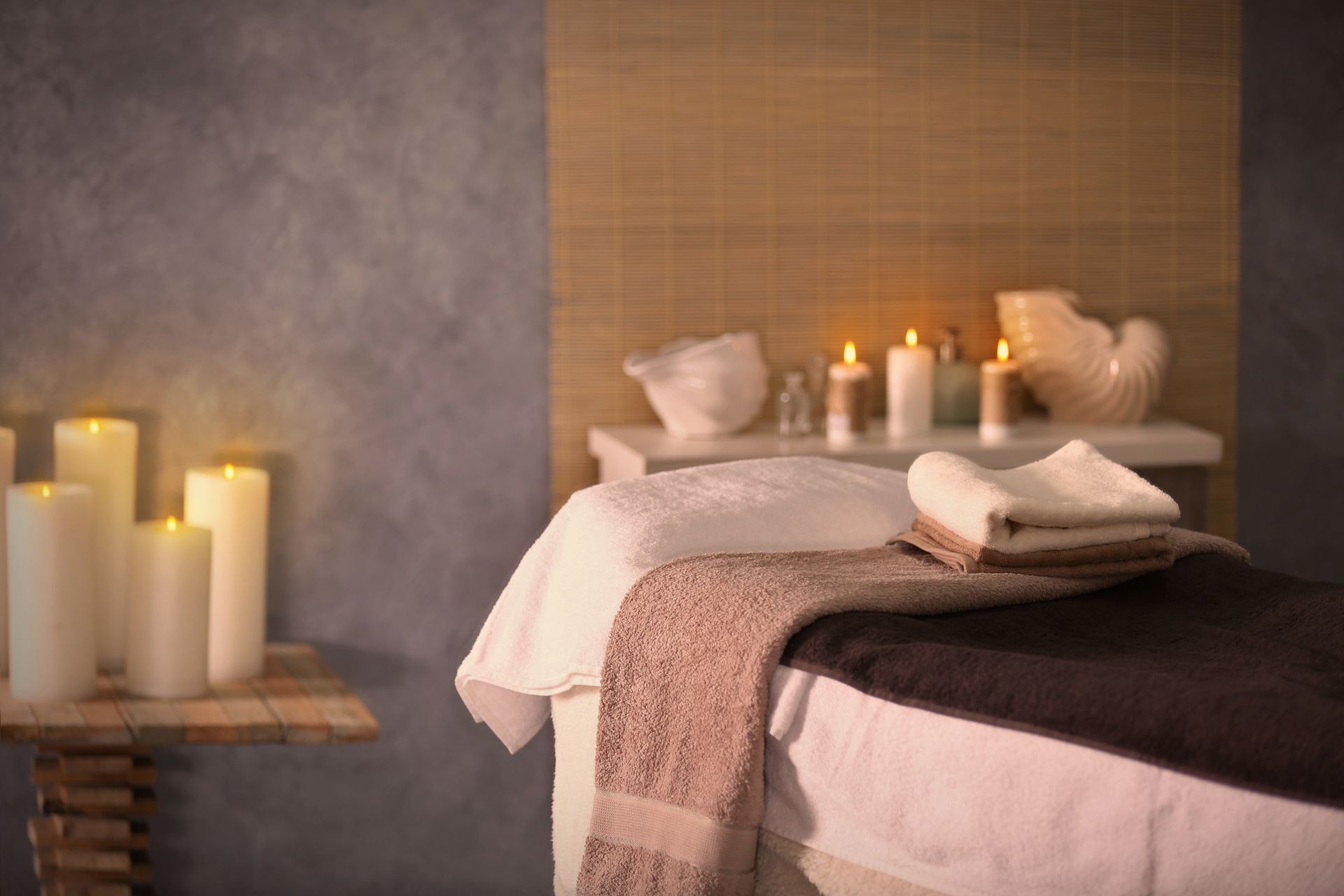 Spa treatment room with lit candles, massage bed, towels, and a folded robe