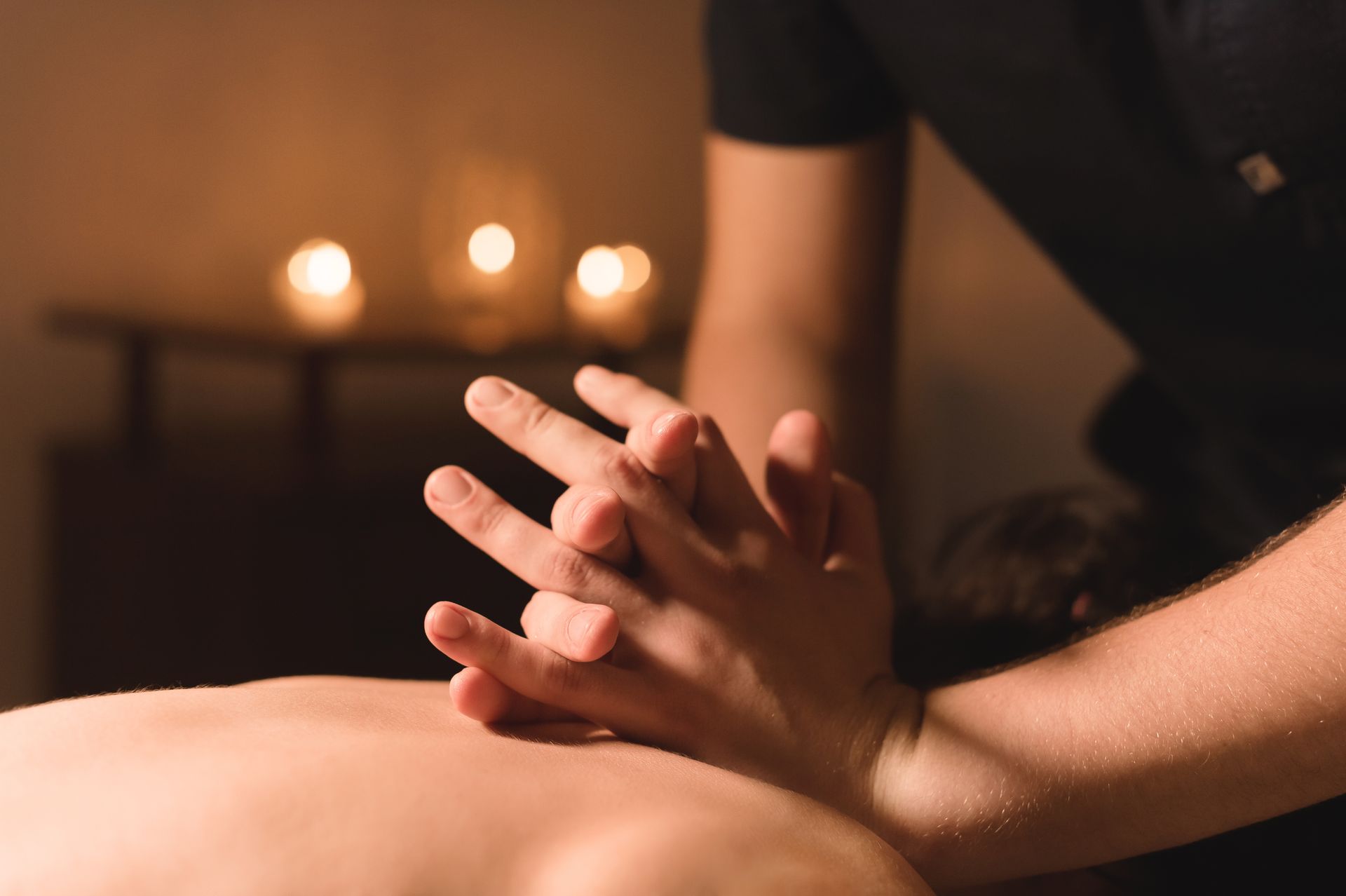 Hands giving a back massage with candles glowing in the background.