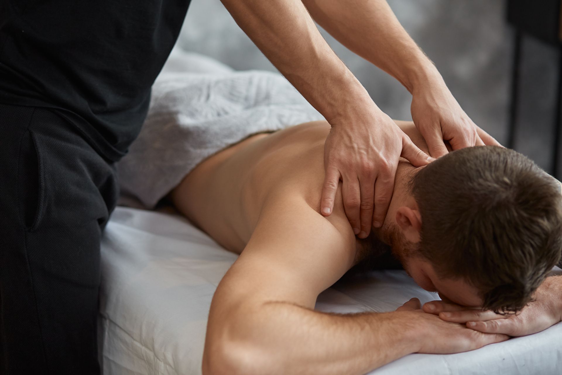 Massage therapist giving a back massage to a man lying face down on a bed
