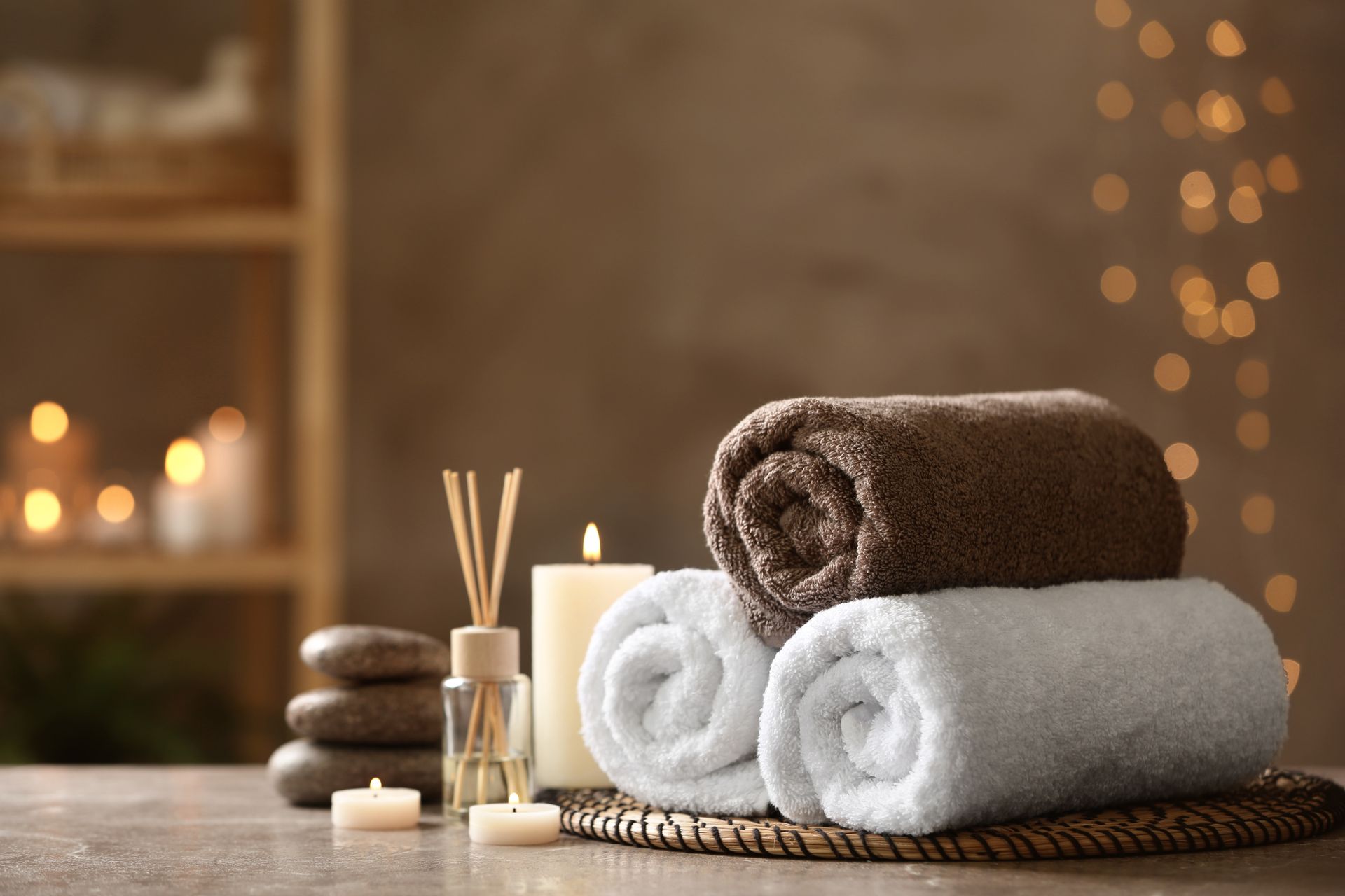 Stacked white and brown rolled towels with candles and reed diffuser in a spa setting