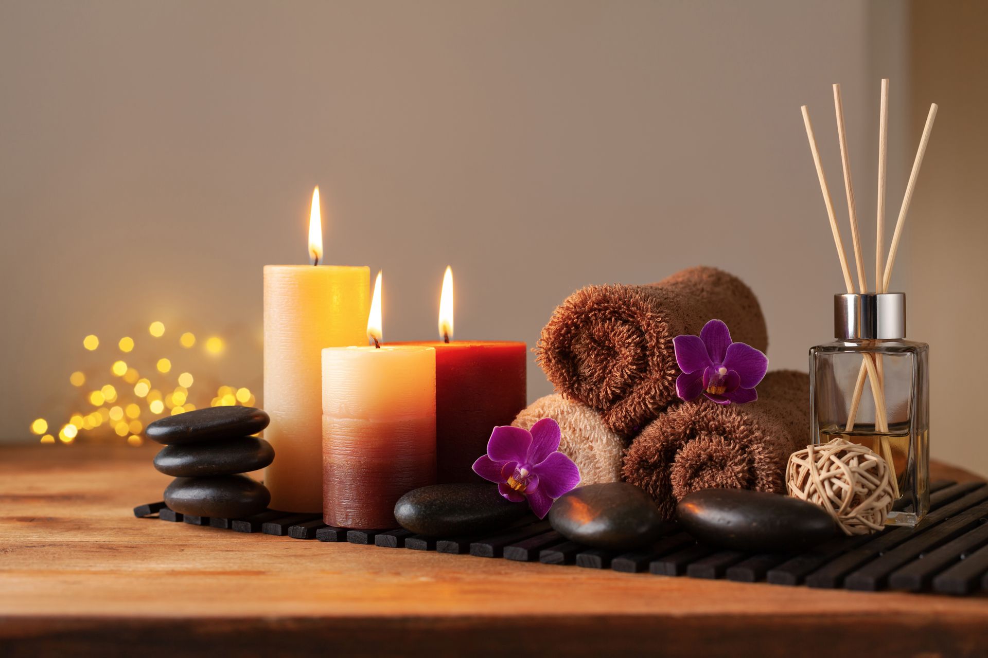 Spa candles, black stones, purple orchid, rolled towels, and incense sticks on a wooden table