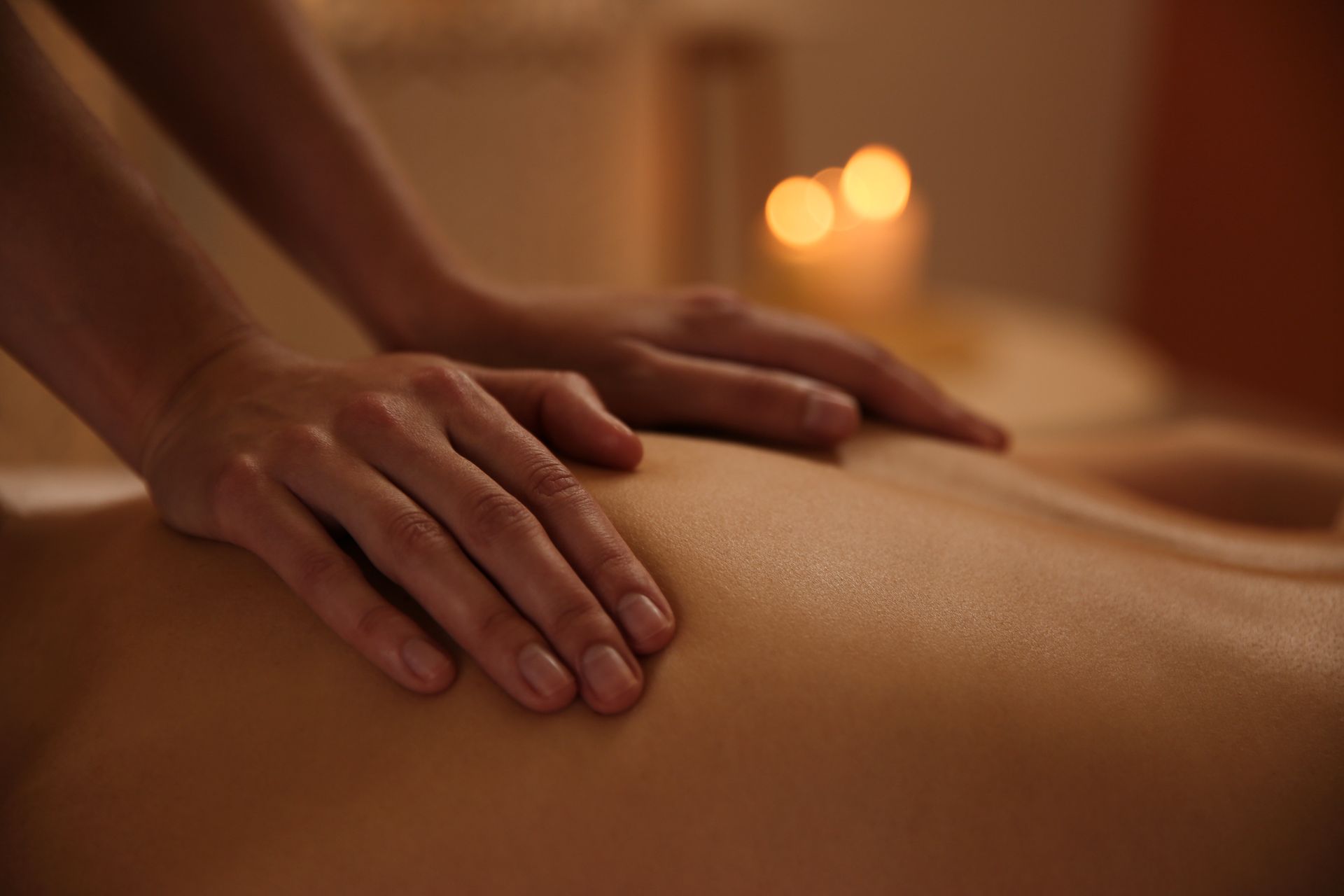 Hands giving a back massage with warm candlelight in a spa setting