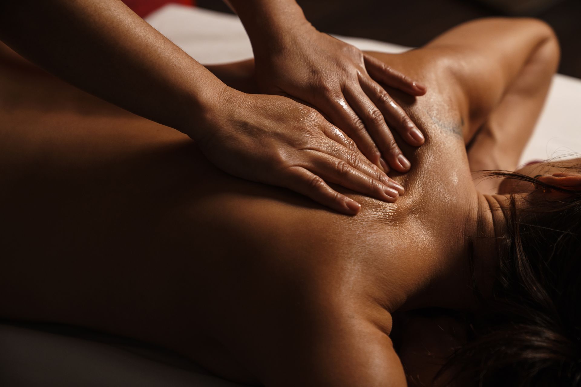 Hands giving a back massage on a person lying face down in a dimly lit spa setting