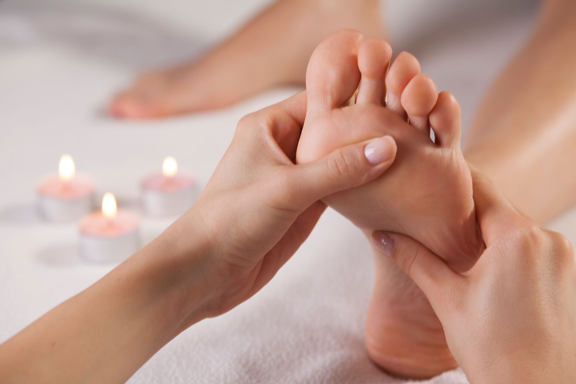 Hands giving a foot massage with lit candles in the background